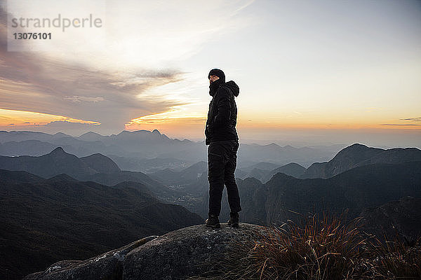 Mann schaut weg  während er bei Sonnenuntergang auf einem Berg steht