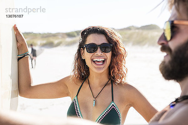 Glückliche Frau unterhält sich bei Sonnenschein mit einem männlichen Freund am Strand