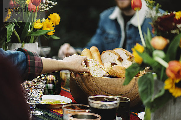 Ausgeschnittenes Bild einer Frau  die Brot aus einer Holzschüssel nimmt  während sie mit einem Freund am Tisch sitzt