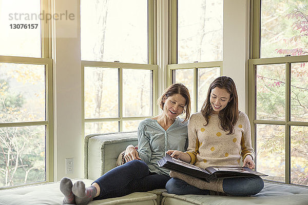 Lächelnde Mutter und Tochter beim Betrachten des Fotoalbums im Wohnzimmer