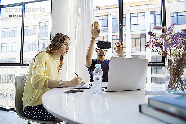 Geschäftsmann nutzt Virtual-Reality-Simulator  während Geschäftsfrau am Tisch im Büro arbeitet