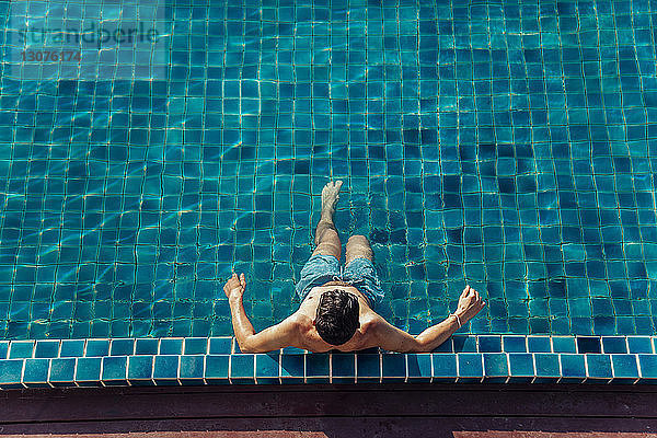 Hochwinkelaufnahme eines Mannes ohne Hemd  der sich im Schwimmbad eines Touristenortes entspannt