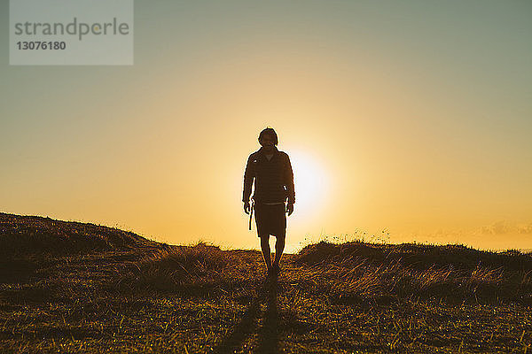 Wanderer in voller Länge auf Grasfeld vor klarem Himmel bei Sonnenuntergang