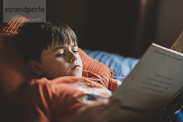 Junge liest Buch  während er zu Hause auf dem Bett liegt