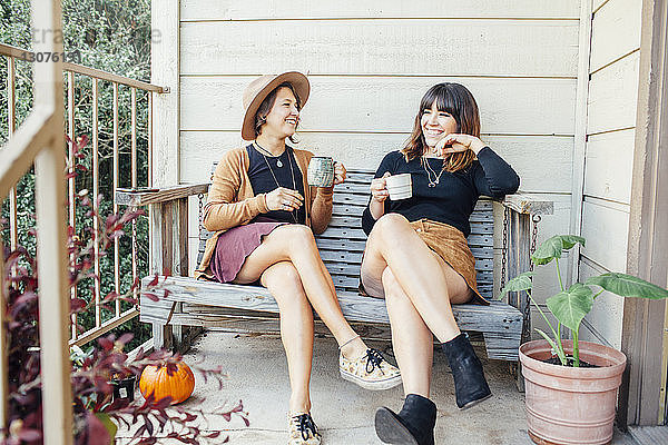 Freundinnen bei einem Drink auf einer Holzbank in der Veranda sitzend