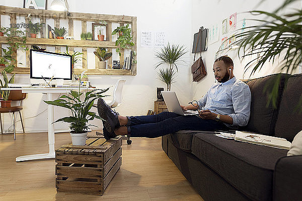 Männlicher Illustrator mit Laptop  während er im Kreativbüro auf dem Sofa sitzt