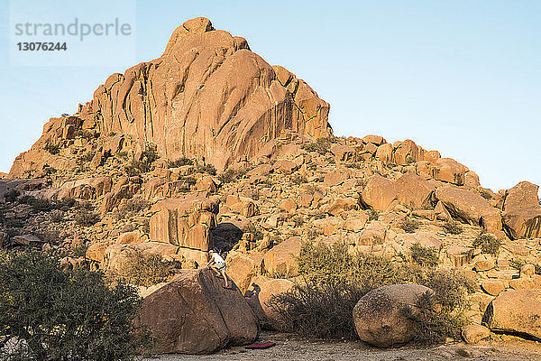 Mann klettert auf Fels gegen Berge und klaren Himmel in der Wüste
