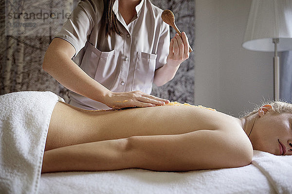 Mittelteil einer Massagetherapeutin  die im Spa Medikamente auf dem Rücken der Frau anwendet