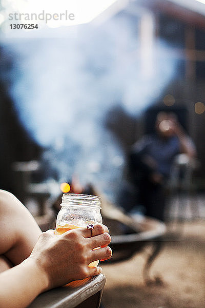 Ausgeschnittenes Bild einer Frau  die ein Getränk in der Hand hält  während sie auf einem Stuhl im Hof sitzt