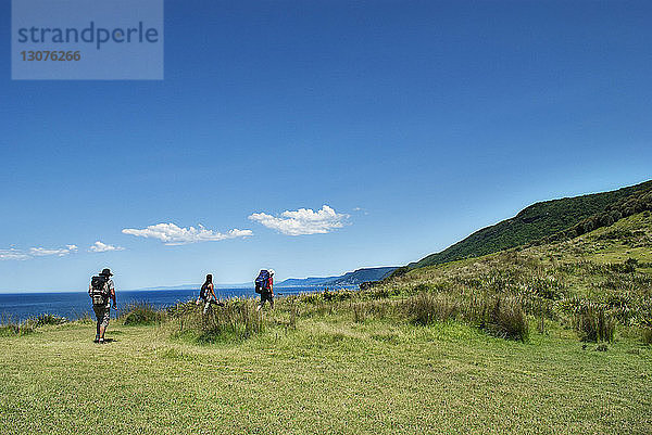 Wanderer erklimmen Berg am Meer vor blauem Himmel