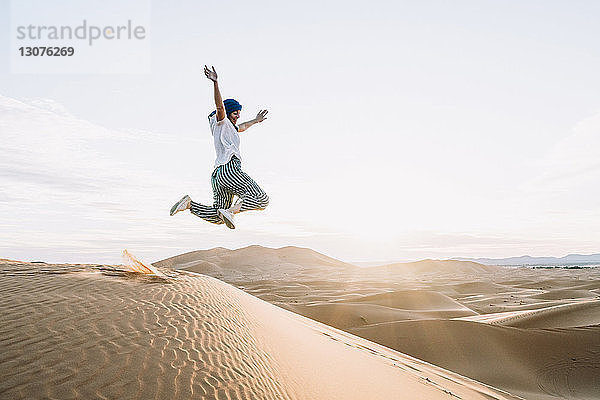 Glückliche Frau springt in der Wüste Merzouga gegen den Himmel