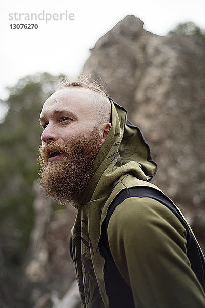 Fröhlicher Hipster mit Kapuzen-Shirt am Hanging Rock stehend