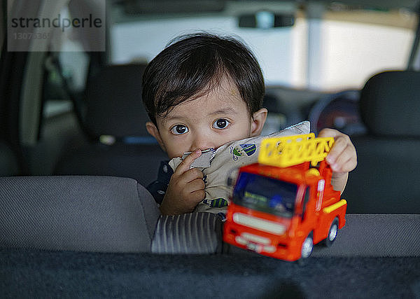 Porträt eines süßen Jungen  der mit einem Spielzeuglastwagen im Auto spielt