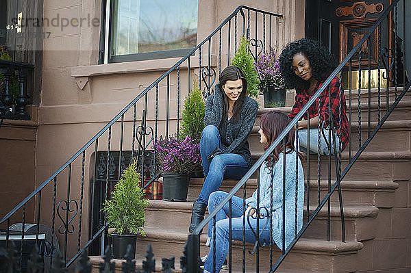 Freunde unterhalten sich  während sie auf Stufen vor dem Haus sitzen