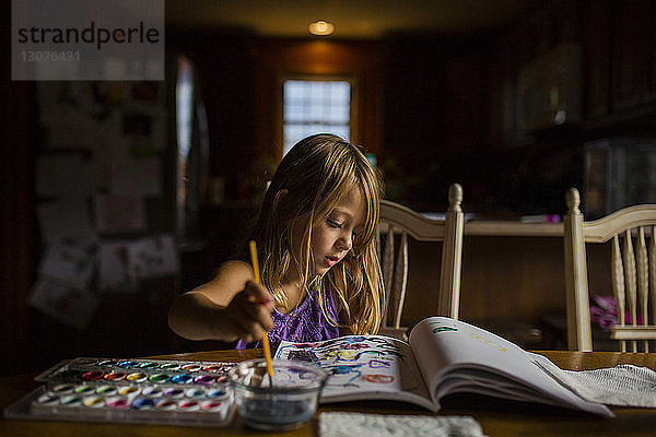 Mädchen zeichnet im Buch  während sie am Tisch sitzt
