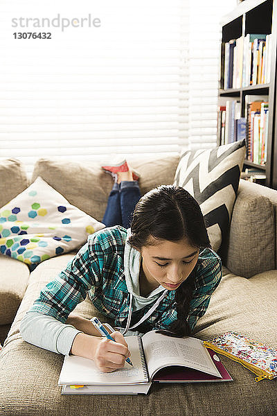 Schwere Teenagerin in voller Länge  die Hausaufgaben macht  während sie zu Hause auf der Couch liegt
