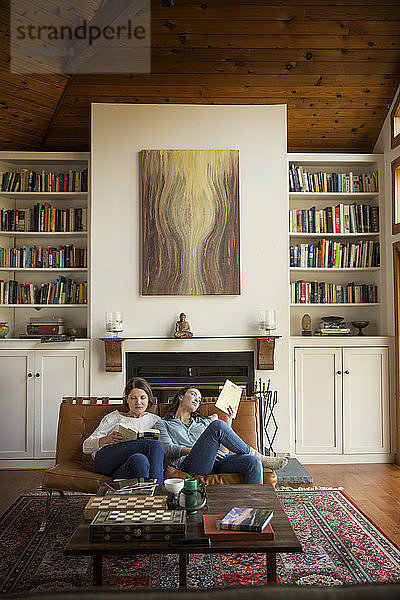 Tochter und Mutter lesen Bücher  während sie auf dem Sofa im Wohnzimmer sitzen