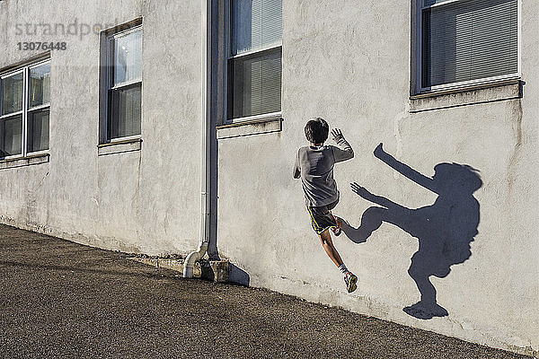 Rückansicht eines Teenagers  der an einem sonnigen Tag über eine Mauer springt