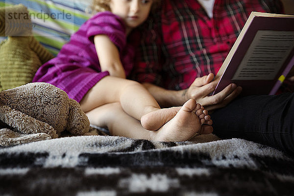 Ausgeschnittenes Bild eines Mädchens  das beim Vater sitzt und zu Hause ein Buch hält