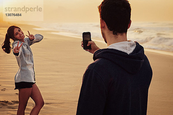 Mann fotografiert seine Freundin am Strand
