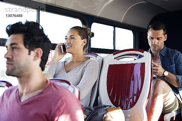 Frau telefoniert mit einem Mobiltelefon  während sie mit anderen Fahrgästen im Reisebus unterwegs ist