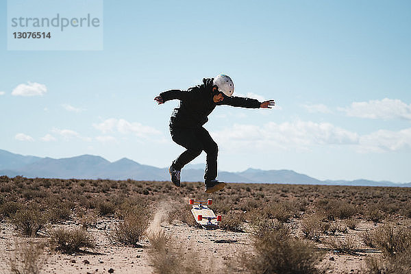 Mann in voller Länge beim Stunt mit Skateboard auf dem Feld gegen den Himmel