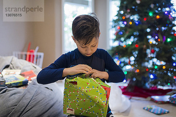 Junge packt Weihnachtsgeschenk ein  während er zu Hause sitzt