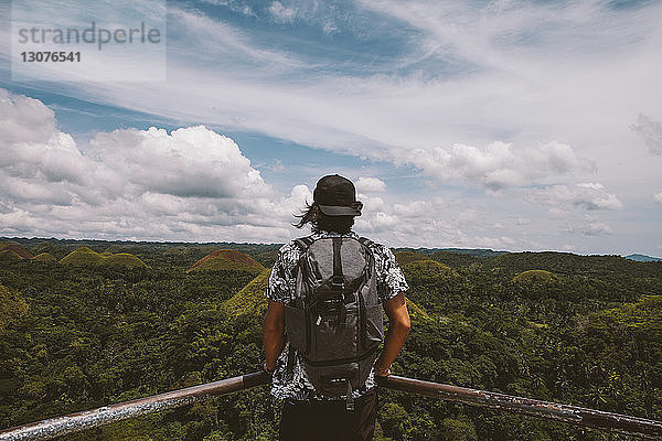 Rückansicht eines Mannes mit Rucksack beim Blick auf Chocolate Hills  der am Geländer steht