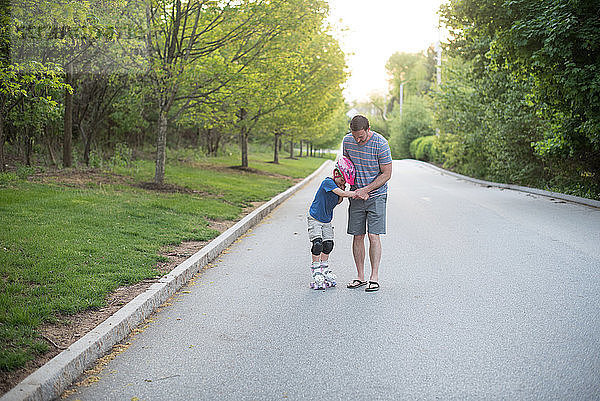 Vater assistiert Sohn beim Rollschuhlaufen auf der Straße im Park