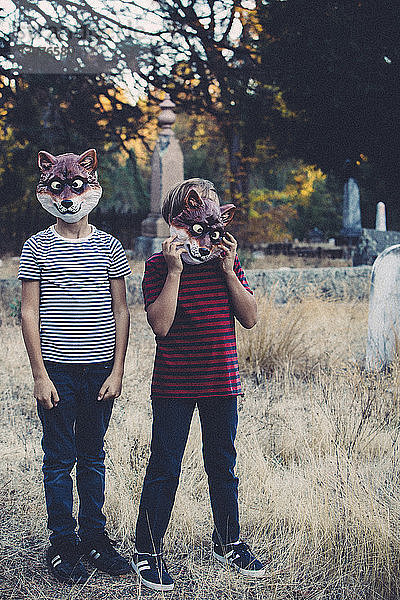 Geschwister tragen Tiermasken  während sie auf dem Friedhof stehen