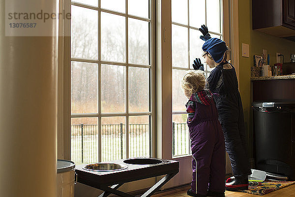 Geschwister schauen durch das Fenster  während sie zu Hause stehen