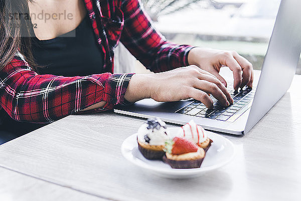 Mittelsektion einer Frau  die einen Laptop-Computer benutzt  bei süßem Essen auf dem Tisch im Café