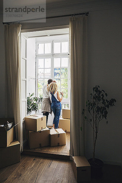 Rückansicht eines Paares  das durch ein Fenster schaut  während es in einem neuen Haus steht  durch eine Tür gesehen