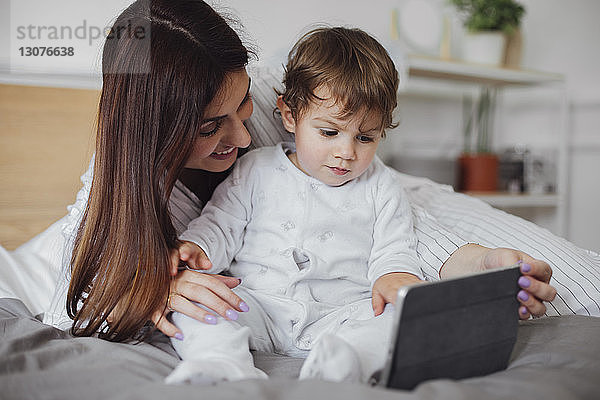 Glückliche Mutter mit Tablet-Computer und Baby-Boy im Bett