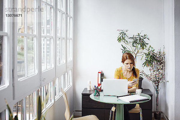 Geschäftsfrau telefoniert am Tisch sitzend mit Laptop im Büro