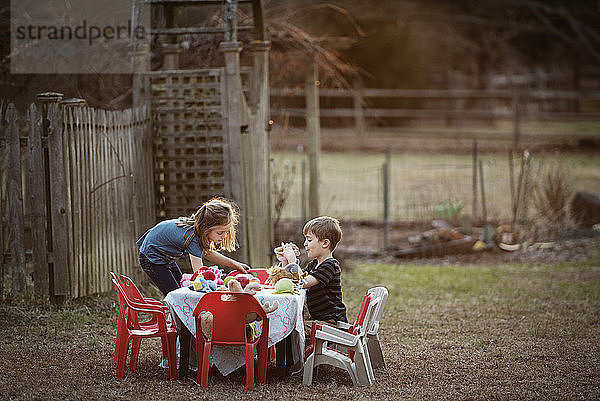 Seitenansicht von Bruder und Schwester beim Essen am Esstisch im Hof