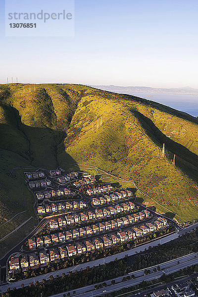 Luftaufnahme von Reihenhäusern in grüner Landschaft vor klarem Himmel