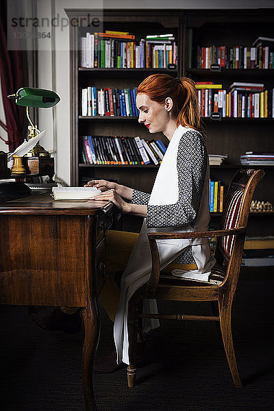 Seitenansicht einer Geschäftsfrau  die ein Buch am Schreibtisch im Kreativbüro liest