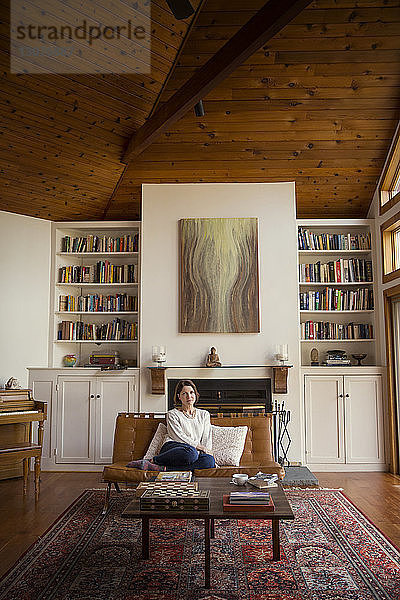 Nachdenkliche Frau sitzt auf Stuhl gegen Regale im Wohnzimmer