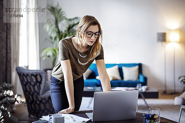Geschäftsfrau betrachtet Laptop  während sie sich im Kreativbüro auf den Tisch lehnt