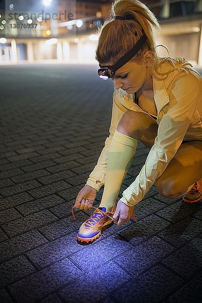 Weibliche Sportlerin bindet nachts auf dem Gehweg die Schnürsenkel
