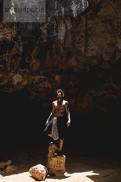 Mann schaut auf  während er auf Felsen in einer Höhle steht
