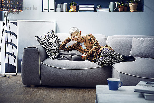 Frau benutzt Tabletten  während sie sich zu Hause auf dem Sofa entspannt