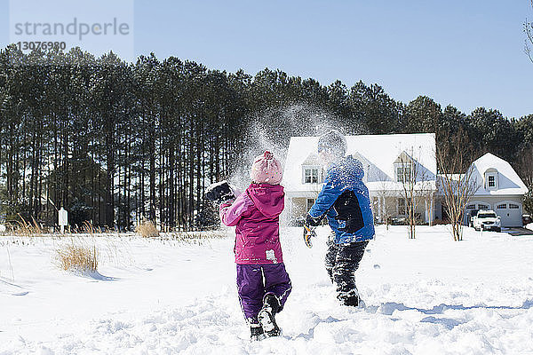 Geschwister spielen mit Schnee auf dem Feld gegen den klaren Himmel