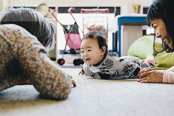 Glückliche Mutter und Großvater spielen zu Hause mit dem süßen kleinen Jungen  der auf dem Teppich liegt