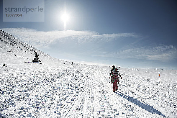 Rückansicht einer Frau  die an einem sonnigen Tag auf einem schneebedeckten Feld gegen den Himmel läuft