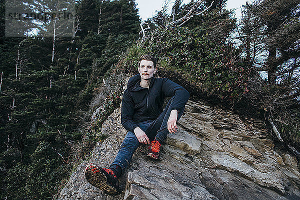 Nachdenklicher Wanderer sitzt auf Fels gegen Bäume