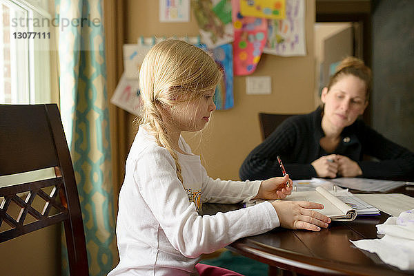 Mutter hilft Mädchen bei den Hausaufgaben am Tisch