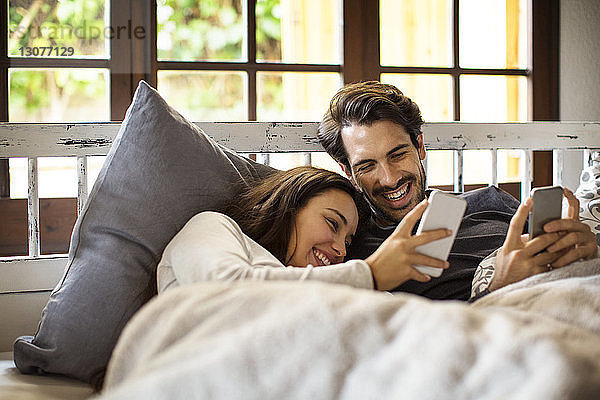 Glückliches Paar benutzt Smartphones  während es zu Hause im Bett liegt