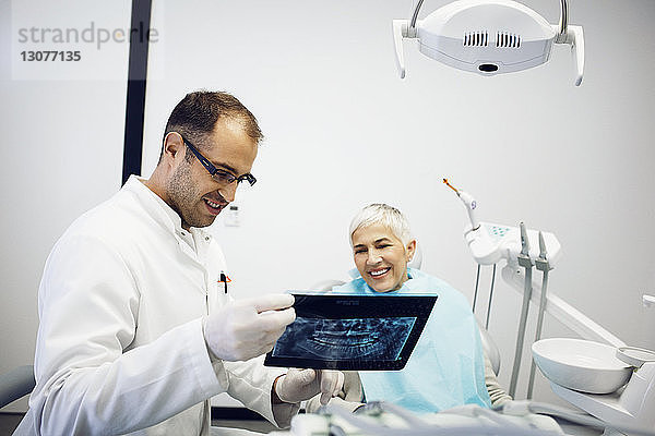 Zahnarzt erklärt lächelnden Patienten in der Klinik das Röntgenbild